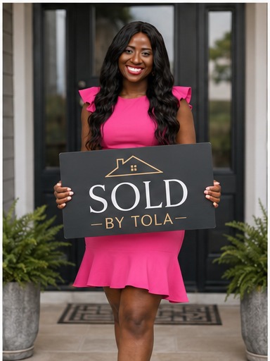 Tola holding a Sold By Tola sign in front of a new home